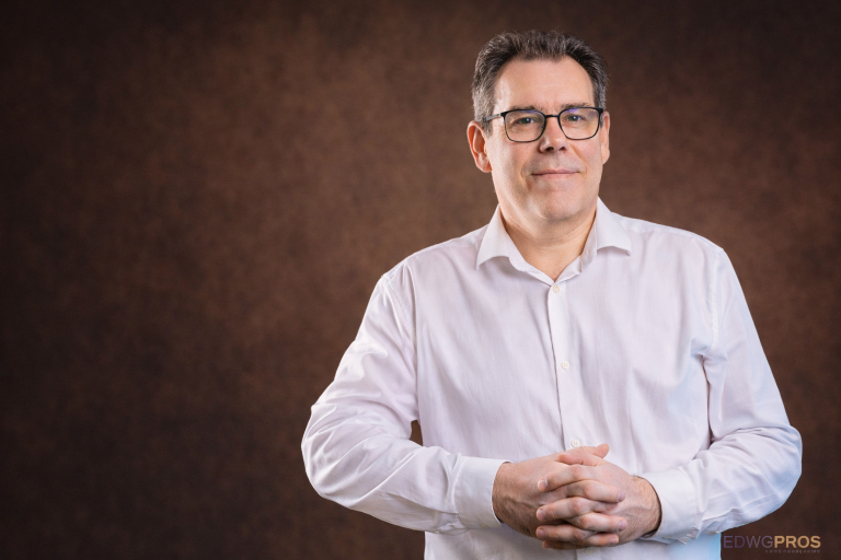 Portrait professionnel de Didier Lourdelle, consultant et formateur, regard face caméra, fond brun.
